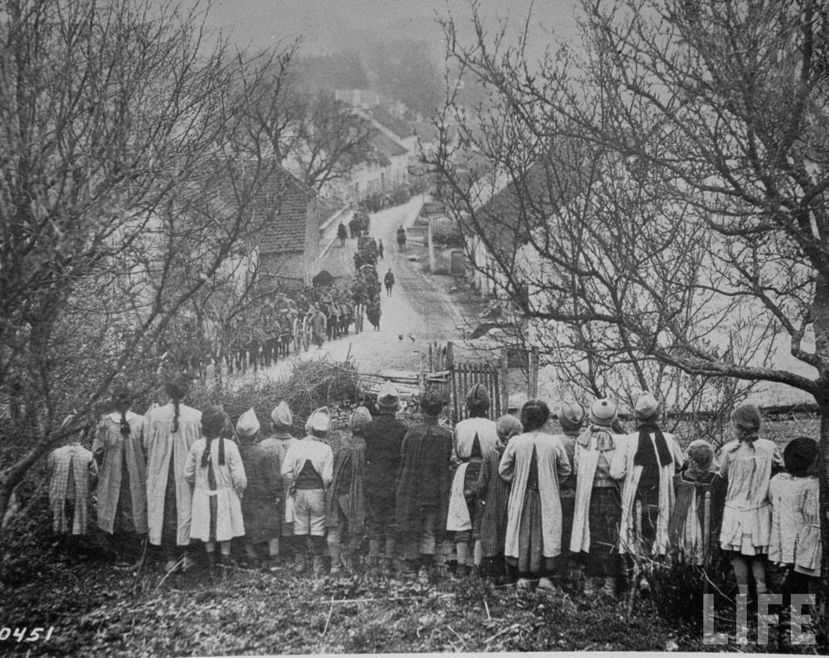 French children watch snaking line of an American ammunition supply train make its way through their village during World War I.
