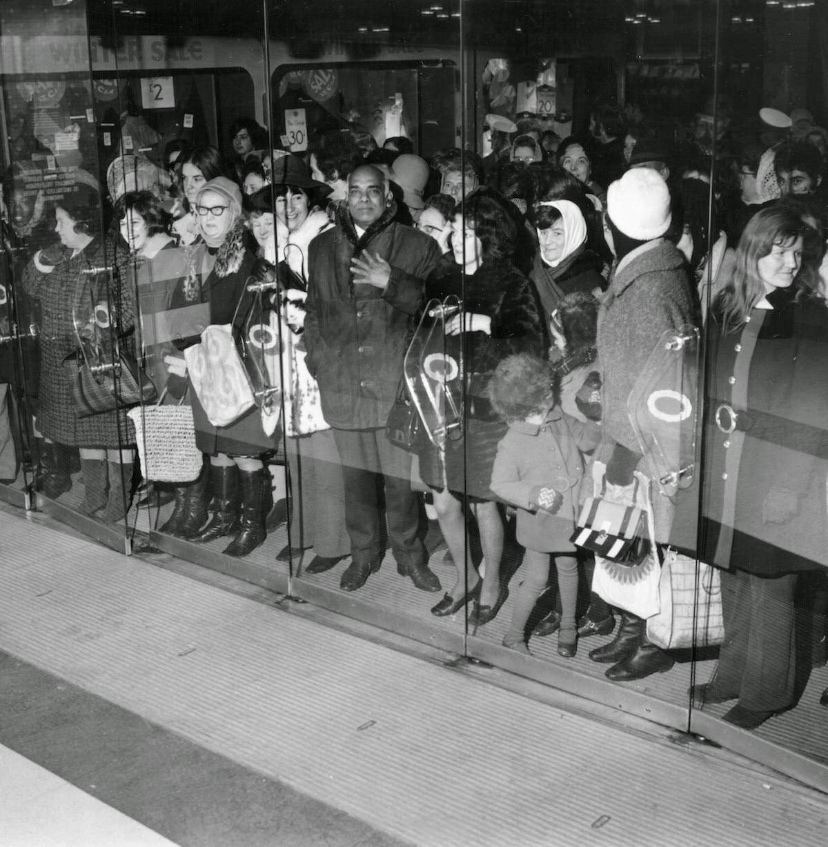 Shoppers waiting behind glass doors for the start of the January sale at C&A on Oxford Street, London, 1970