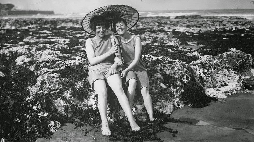 Two bathers sitting on the rocks at Broadstairs beach under a parasol, 1928