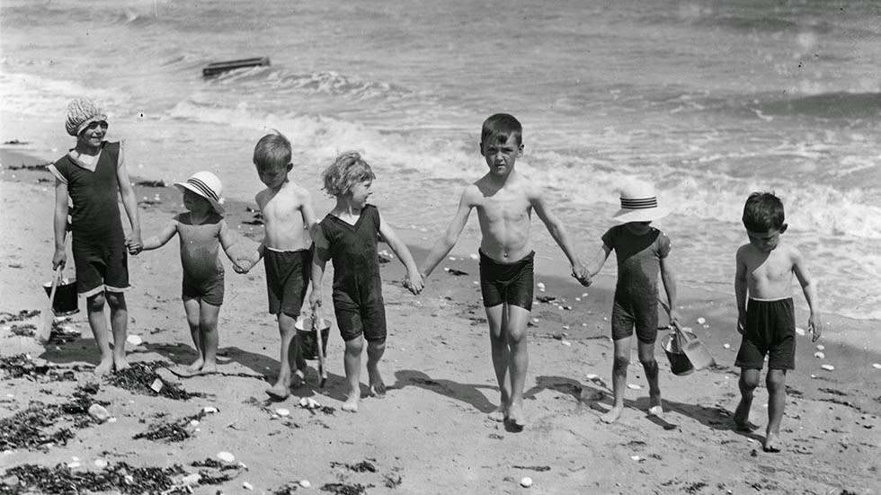 Group of young children walking hand in hand by the sea, 1928