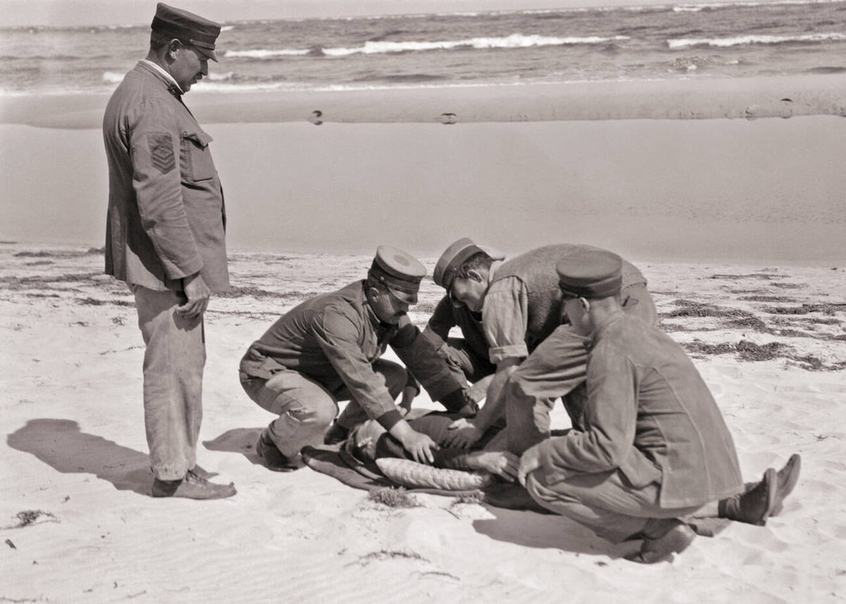 Coast Guard petty officer supervising a crew rendering first aid to a man on a beach in New Jersey, 1915