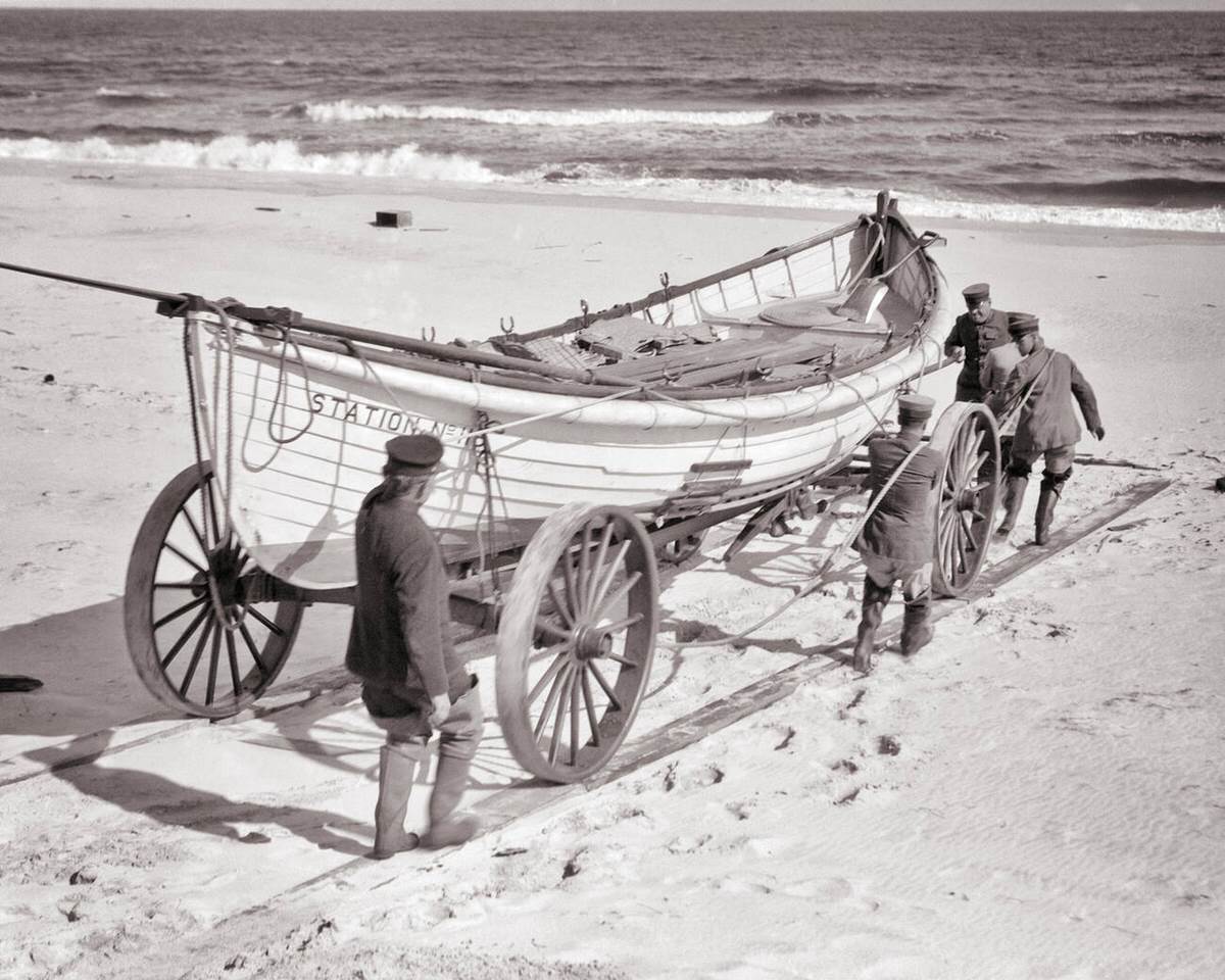 Coast Guard men moving a life-saving surf boat across the sand on a wheeled carriage in New Jersey, 1915