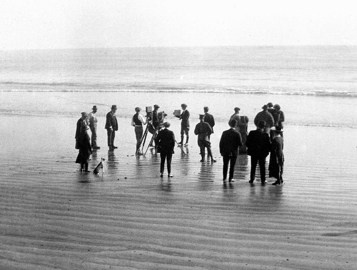 Film crew and a dog working on a California beach, 1925