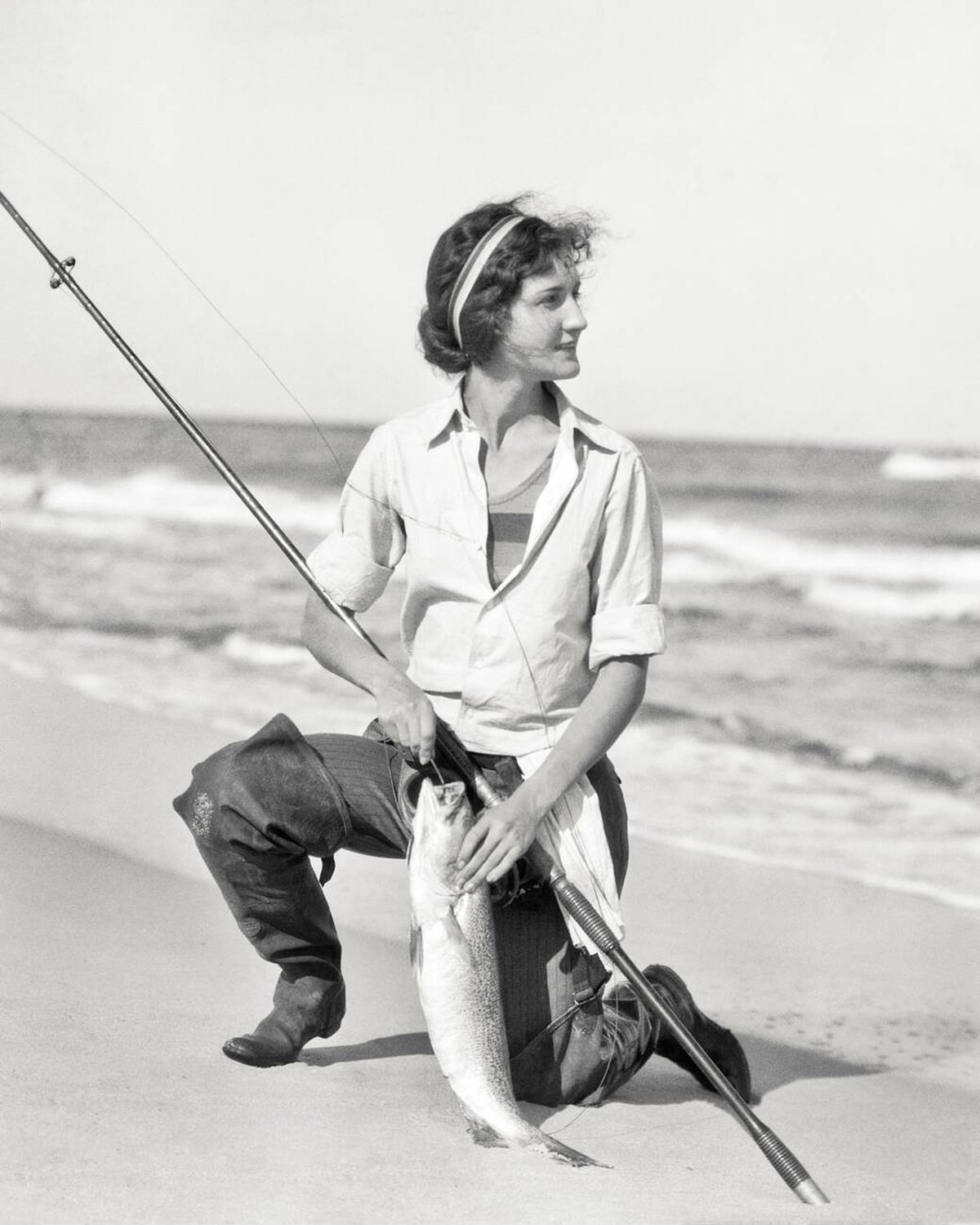 Woman kneeling on the shore with a weakfish caught while surf fishing in New Jersey, 1927