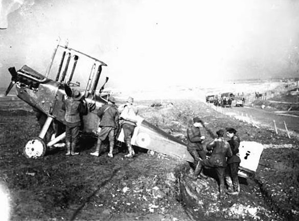 A few soldiers gather round an aeroplane. Three of them are looking at the cockpit, while three others perch near the tail. According to the original caption, these men are dismantling the plane. There are no wings attached which suggests they have either been removed or have suffered severe damage during combat. This photograph is bathed in a bright atmospheric light.