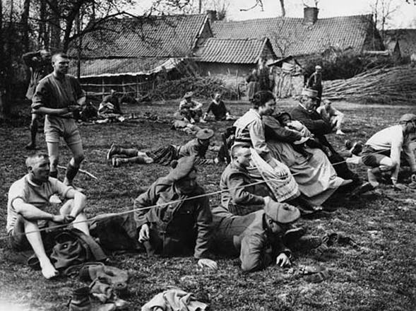 A crowd of onlookers at a sports day organised by the Black Watch Regiment. The spectators include some of the competitors, members of the Black Watch who were not taking part and a number of women and children, possibly from a nearby farm, town or village. A day such as this would have provided some light relief for those at the Front.