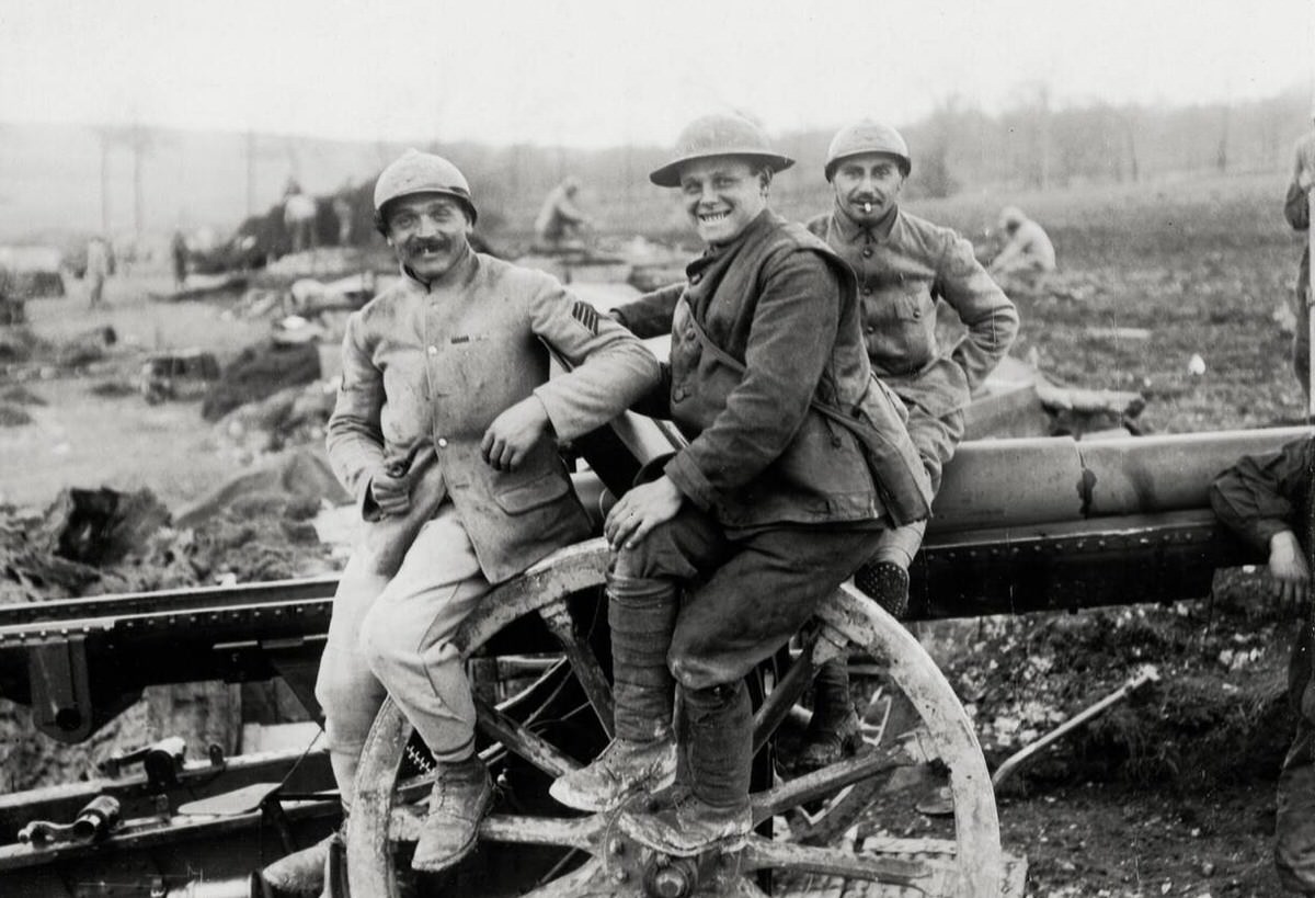 British and French soldiers sitting on the wheel of a French gun in France, 1914