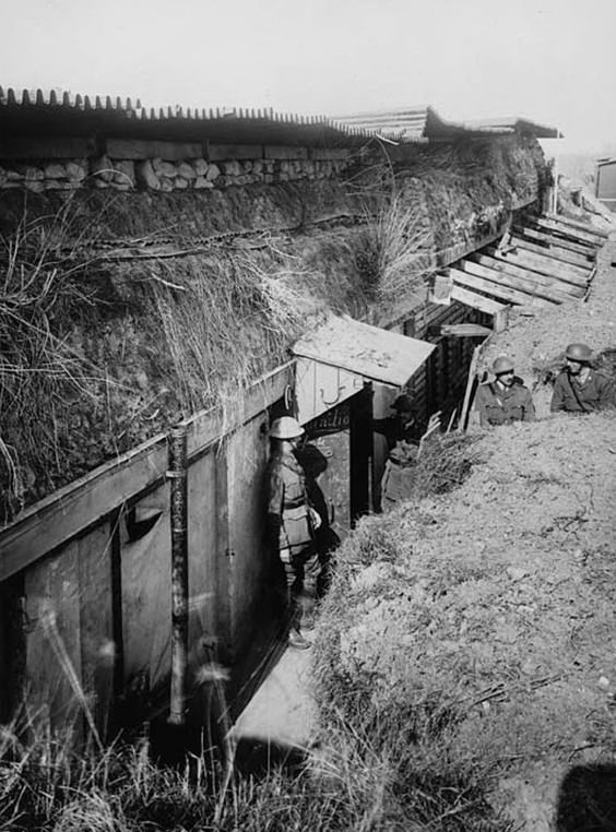 German General's Headquarters' dug-out being used by the British. The concrete on the tops is 10 feet deep. This photograph shows how well-engineered some of the German trenches were. The caption notes that there was 10 feet of concrete on top and the image shows a great depth of concrete and sod below the corrugated iron roof. Drain pipes and even porches can be seen in the dugout.