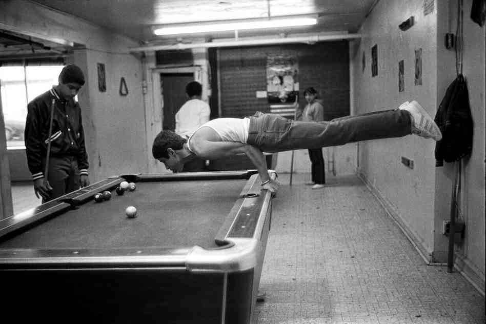 Martin, a teenager, shows his muscles by doing a pushup on the pool table, 1980s.