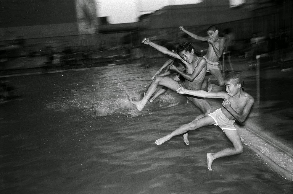 Teenage boys jump into a public swimming pool at night. They climbed over the fence, 1984.