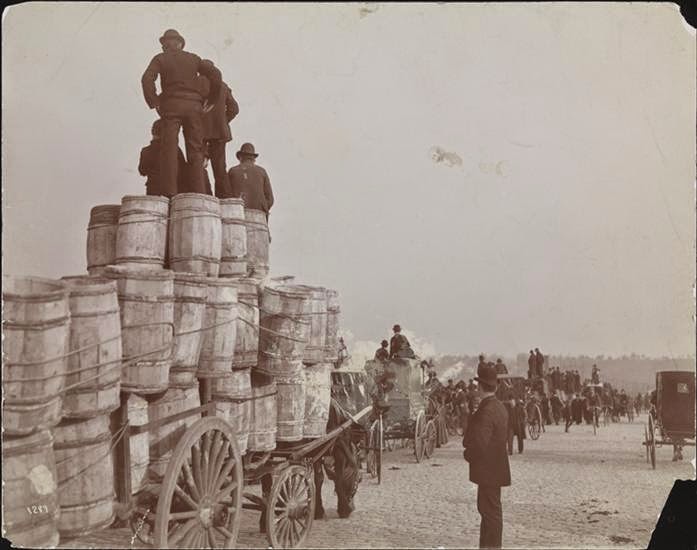 Men standing on carts and barrels on the Harlem River Bridge overlooking Manhattan Field during a football game, 1895