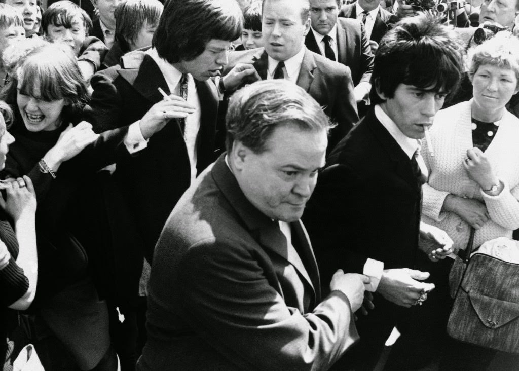 Longhaired Mick Jagger, left center, holding cigarette, and Keith Richard, right, smoking cigarette, leave Chichester, England court, May 10, 1967 after electing to be tied by jury on drug possession charges.