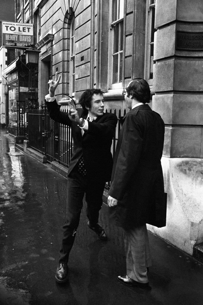 Johnny Rotten, lead singer with the Sex Pistols, giving a double V-sign to journalists after he had been fined £40 on a drugs charge at Marlborough Street Magistrates Court, London. Date: 11/03/1977.