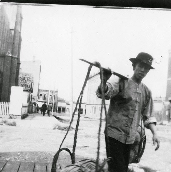 Man on a street carrying yoke with basket, 1897.