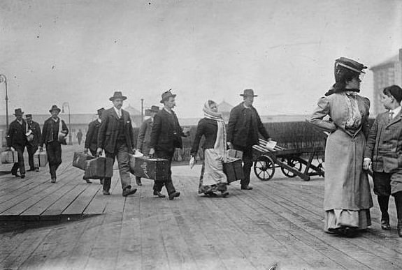 Immigrants carrying luggage at Ellis Island.
