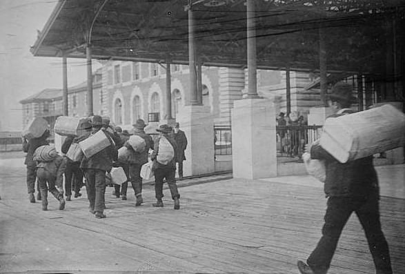 Immigrants carrying luggage at Ellis Island.