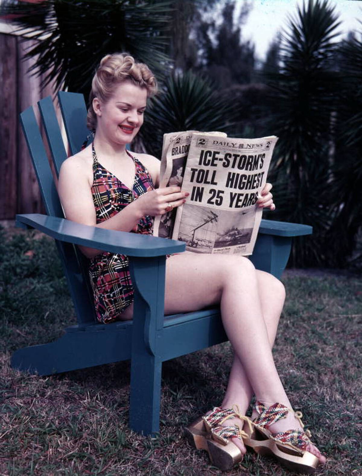 Woman in Sarasota reading about winter storms while sitting in an Adirondack chair, 1940s