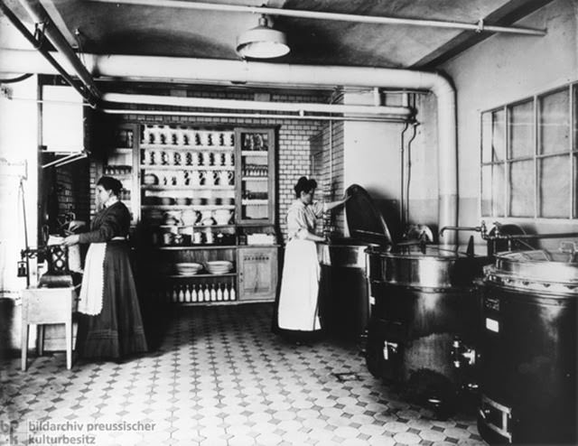 Coffee canteen at AEG, 1909. This canteen in the large-machine factory [Großmaschinenfabrik] of the AEG [Allgemeine Elektizitäts-Gesellschaft or General Electric Company] provided coffee for the entire workforce. The woman on the left measures out beans from a sack; the woman on the right checks one of many large vats of coffee.