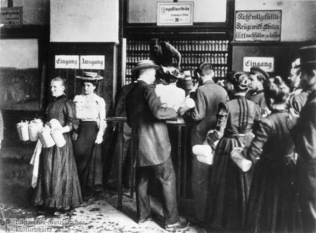 Augustiner brewery, Munich, c. 1910. Breweries were common locales for socializing, especially in Bavaria. Accommodating hundreds of guests, they were prototypical experiments in mass gastronomy, and their appeal transcended class barriers. Here we see customers lining up to order beer by the Maß – i.e., in large 1-liter mugs. Note that the Kellnerin [waitress] to the far left is carrying eight of these mugs to a table; each mug weighed over a kilogram (2.2 pounds), but this was a common feat in these locales. The Augustiner brewery’s summer beer is advertised on the sign above the filling window. Another sign to the right of it reminds customers to make sure their mugs are completely full when picked up: “Mugs not completely full should be topped off immediately.”