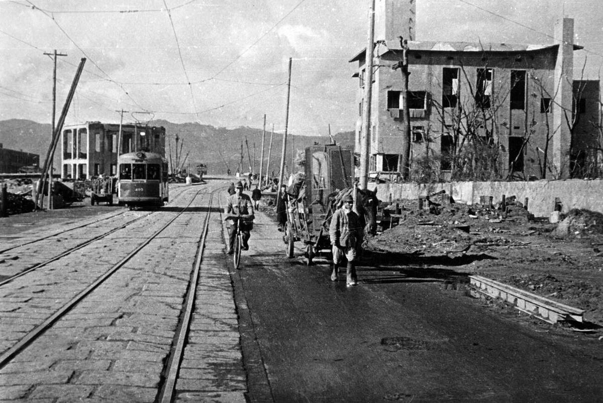 Man pulling furniture on a cart past a streetcar in post-bombing Hiroshima, 1945