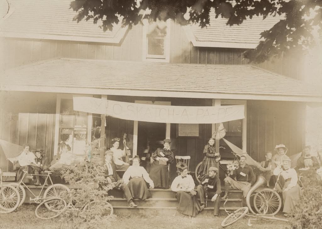 Fifteen men and women seated on a porch with musical instruments, 1897