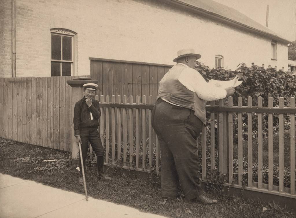 Boy holding a stick contemplating hitting a man reading a newspaper, 1890