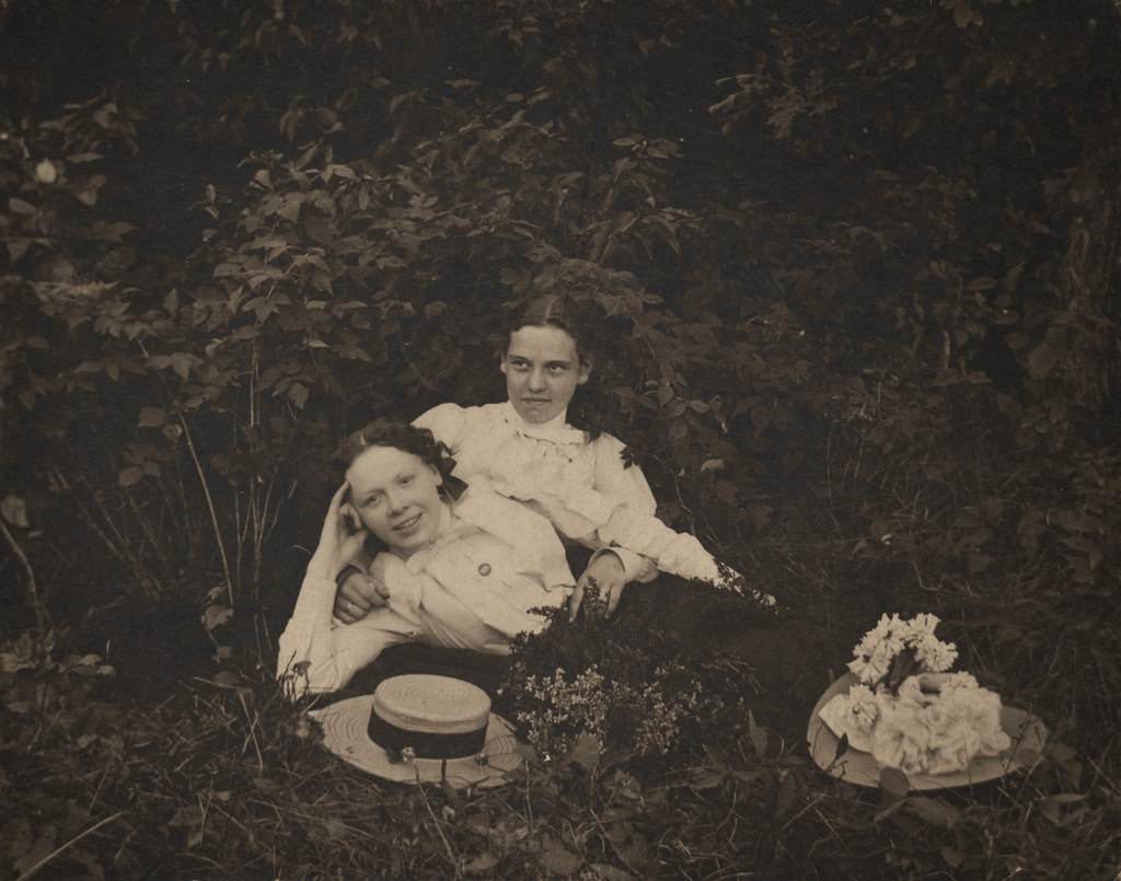 Two women lying among foliage wearing long-sleeved blouses, 1890s