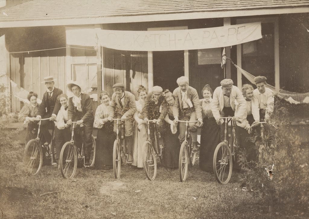 Group portrait of fourteen men and women with men seated on bicycles, 1897