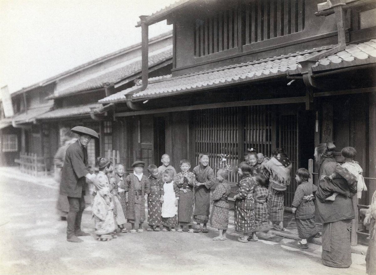 Japanese children in kimono posing before a traditional house, 1870