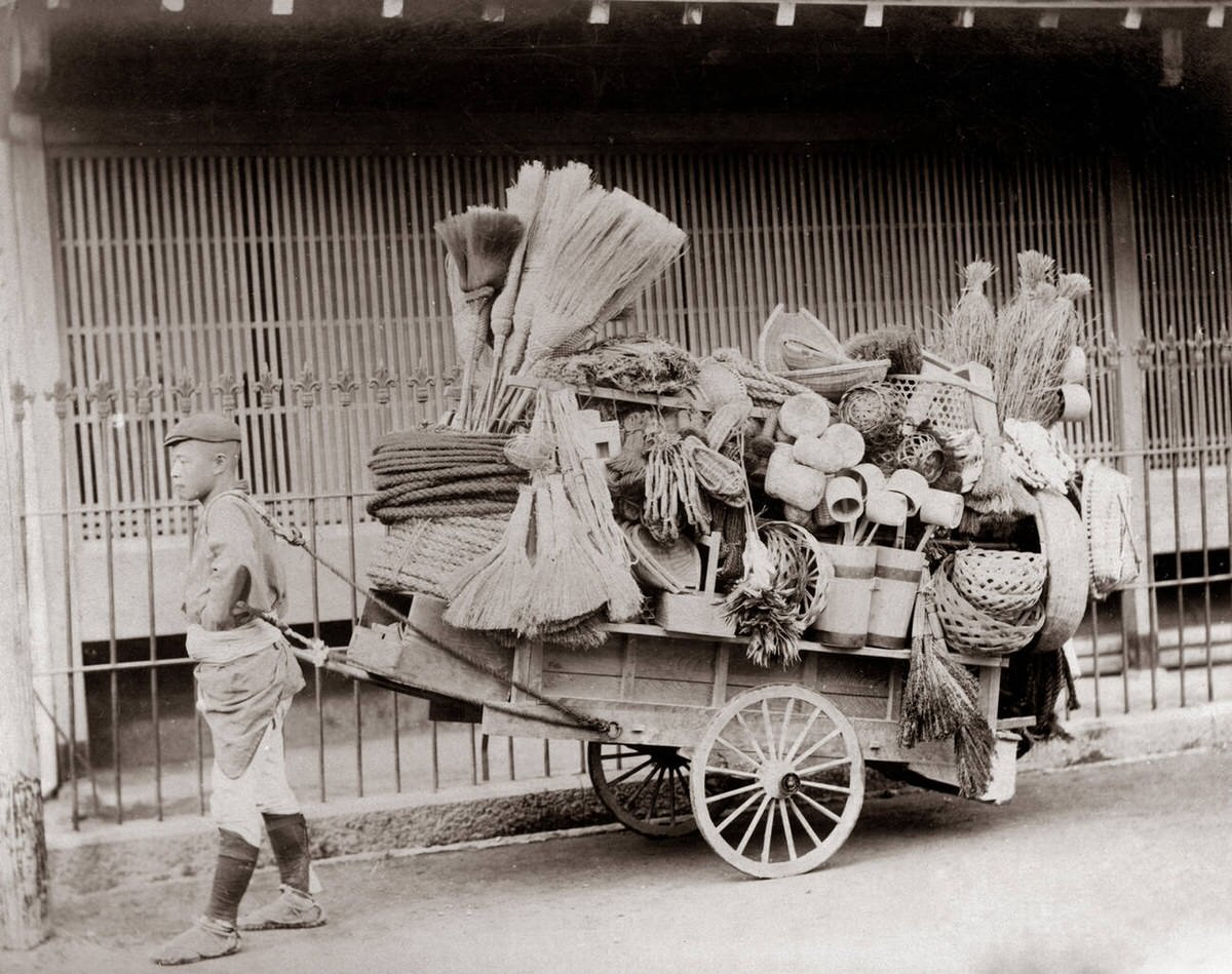 Street vendor pulling a cart with baskets and brooms, 1880s