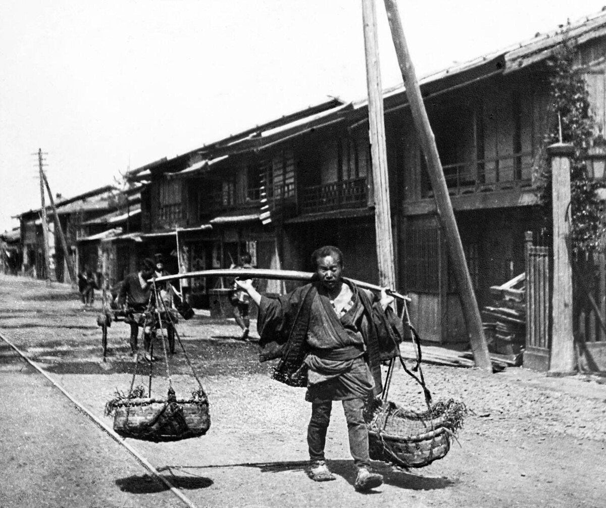 Street vendor carrying baskets of vegetables, 1890s