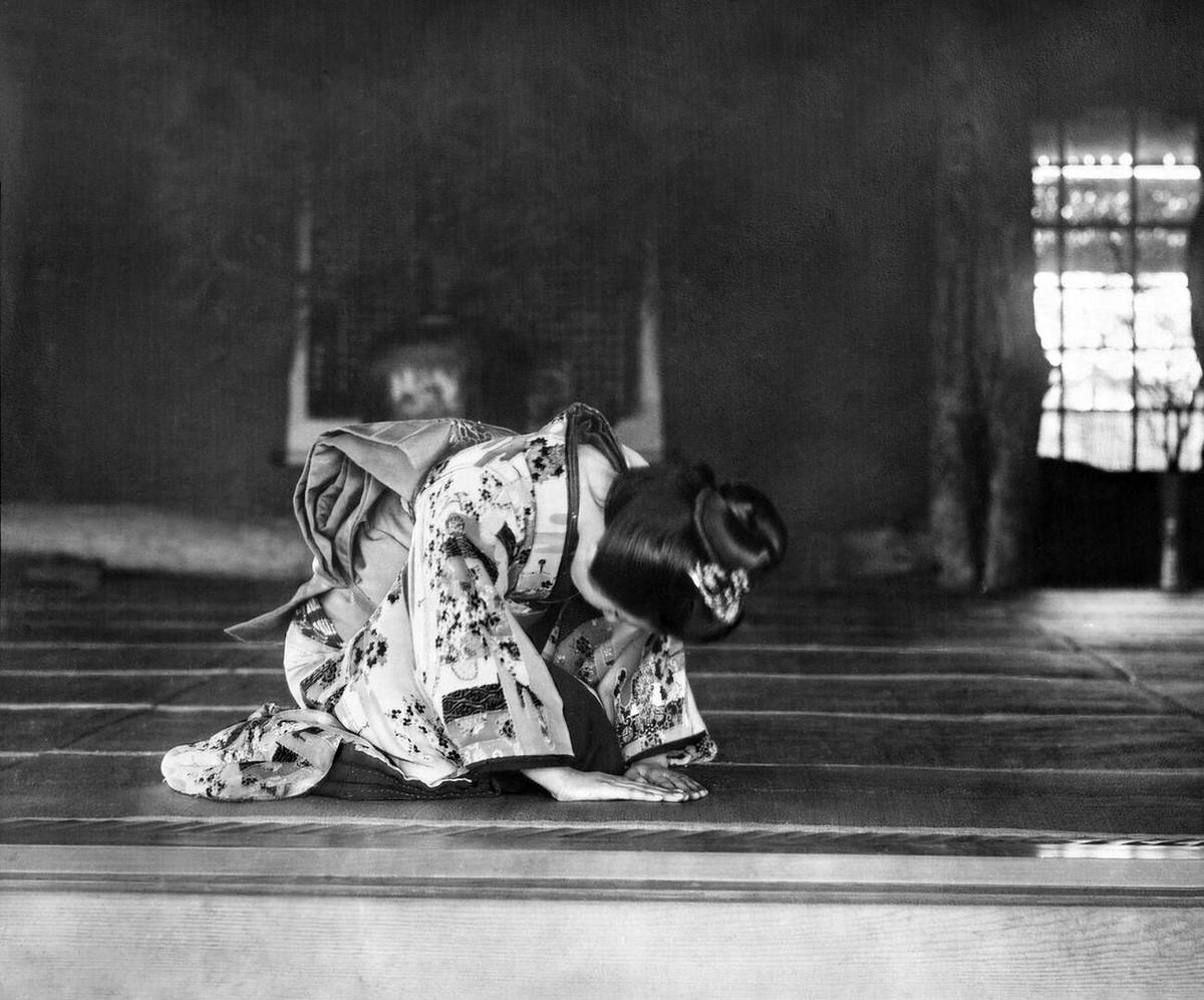 Woman in kimono bowing to receive a guest in a traditional room, 1890s