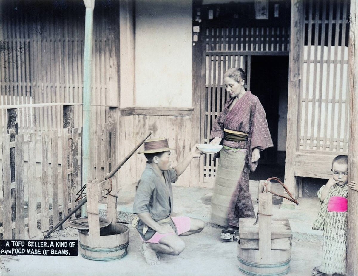 Tofu vendor handing a block of tofu to a customer, 1890s