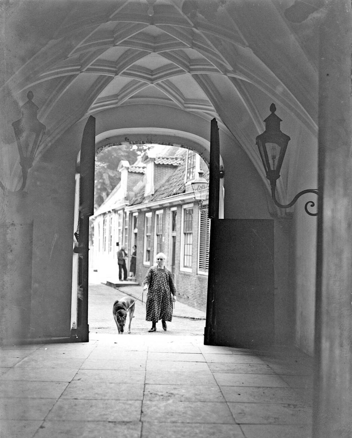 Sexton woman with a dog seen through the doors of the Grote Kerk in Edam, 1932