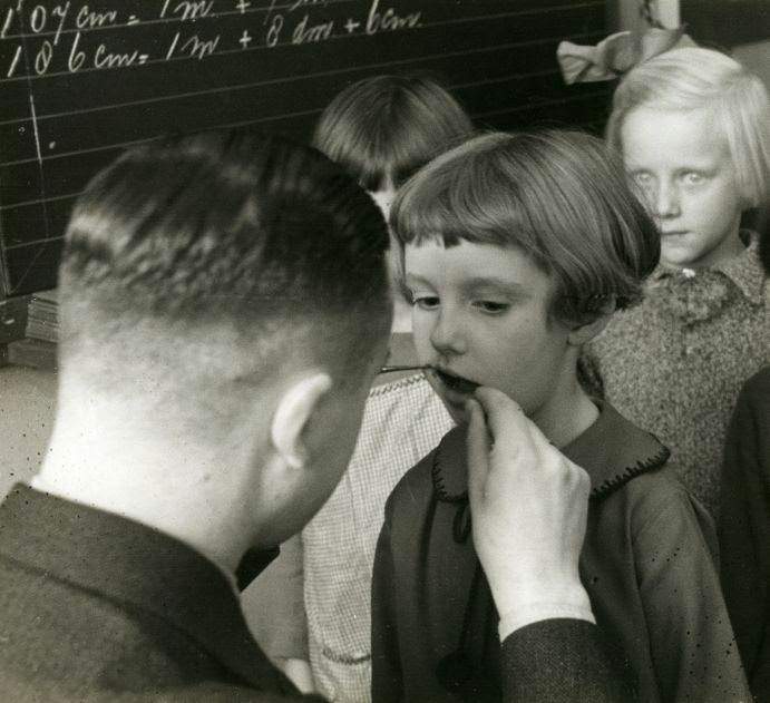 School dentist examining a school girl in the class room. The Netherlands, 1935.
