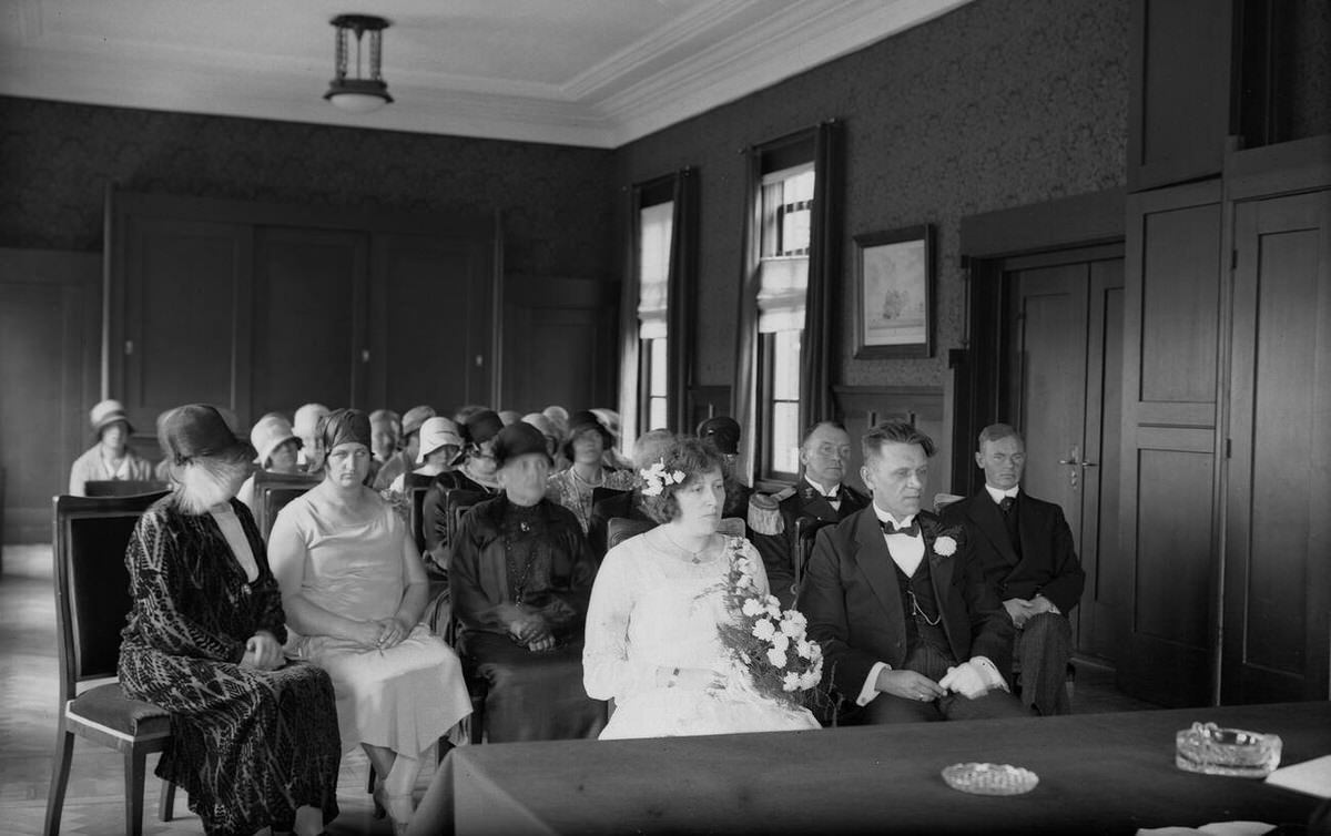 City hall wedding room with a bridal couple and guests during a civil ceremony, 1930