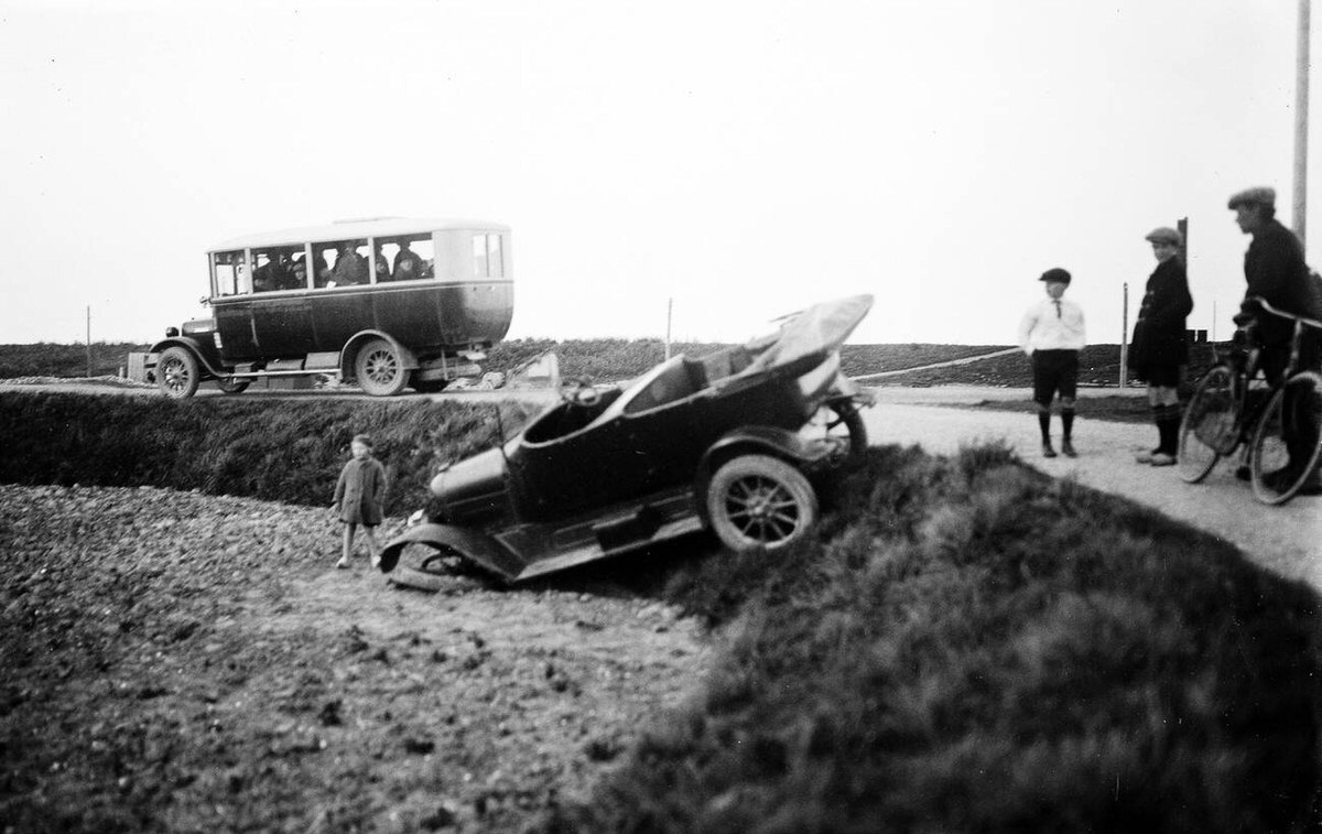 Traffic accident with a passenger car next to a road with a passing bus, 1930