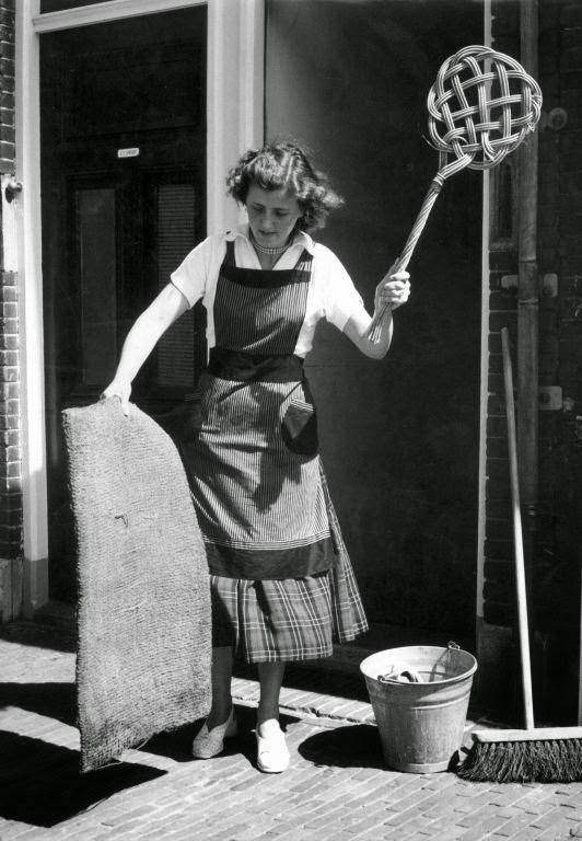 Housewife cleaning doormat with carpet-beater. The Netherlands