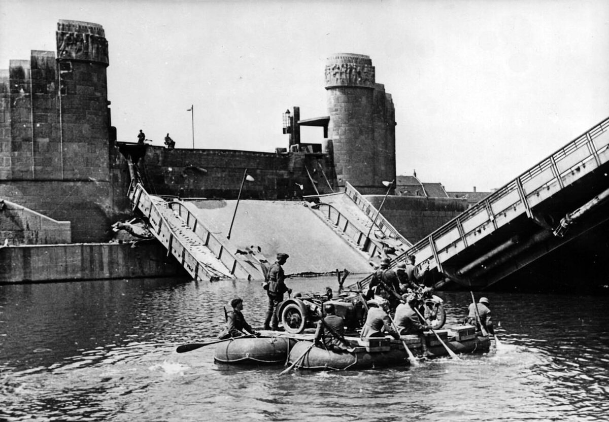 German Wehrmacht soldiers crossing the Meuse river in dinghies near the destroyed Wilhelmina Bridge in Maastricht, 1940