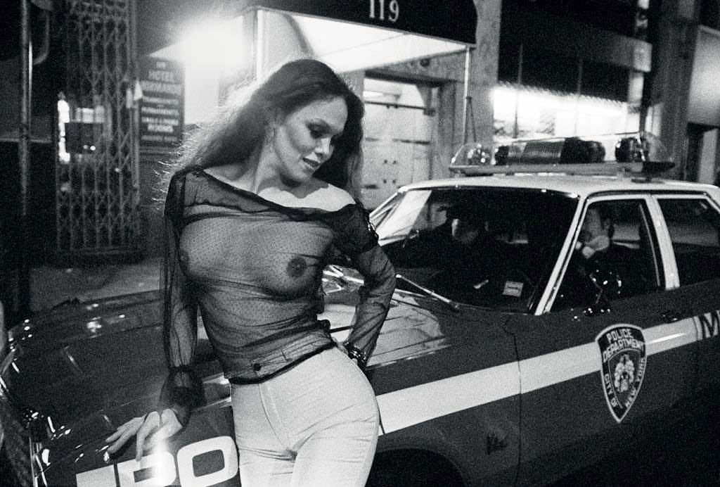 A prostitute leans playfully on a cop car on 42nd Street Times Square, May, 1980. The police struggled to keep up with the onslaught of crime in the area, and at times seemed to be playing a friendly game of cat and mouse with the hookers.