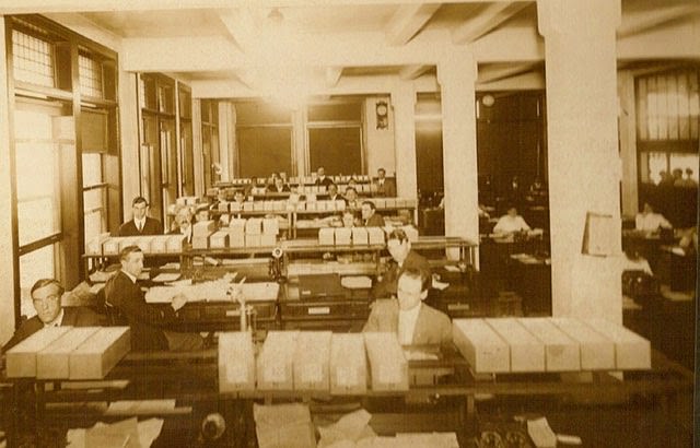 Office with men doing paperwork and women typing.