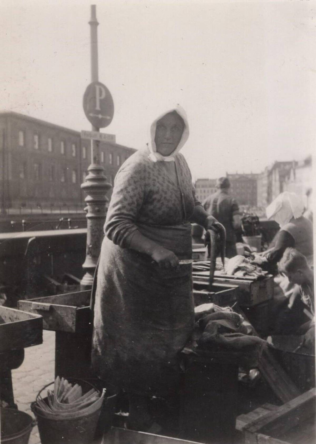 Fishmonger holding an eel and a knife at a fish market, 1930