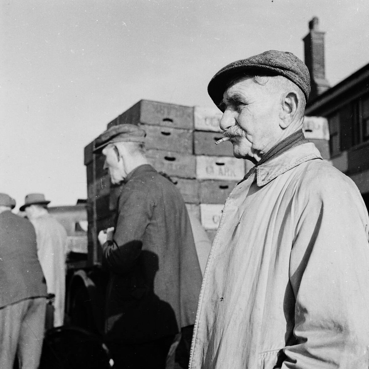 Elderly market trader standing by crates at Billingsgate Fish Market on Lower Thames Street, 1950s