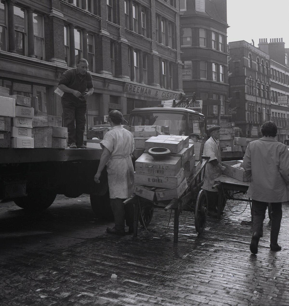 Porters unloading crates from a truck on the wet cobbles of Lower Thames Street, 1950s