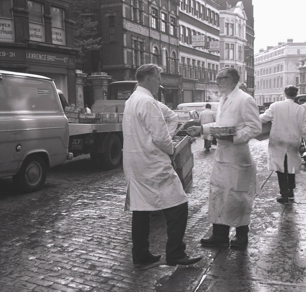 Two fish merchants chatting on a cobbled street outside Billingsgate Fish Market, 1950s