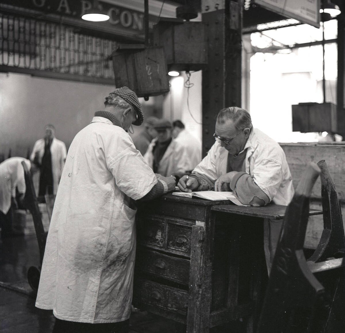 Two fishmongers in white coats writing up sales at Billingsgate Fish Market, 1950s
