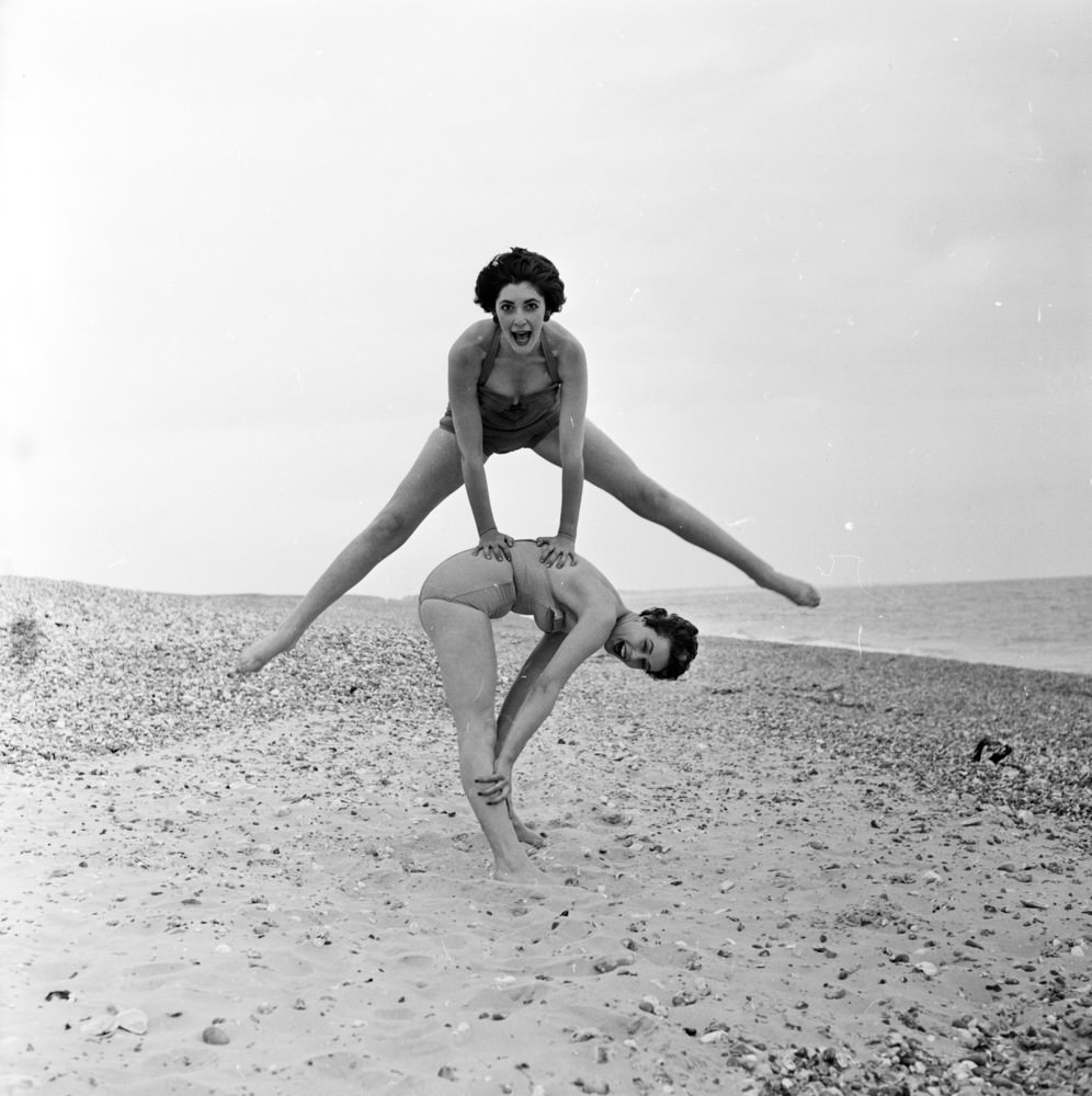 Fashion models Darien Leigh and Valerie Drew playing leapfrog on the beach, 1956