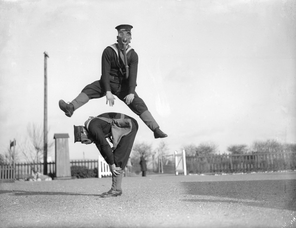 Able seamen at the Royal Navy Anti-Gas School playing leapfrog while wearing gas masks, 1934