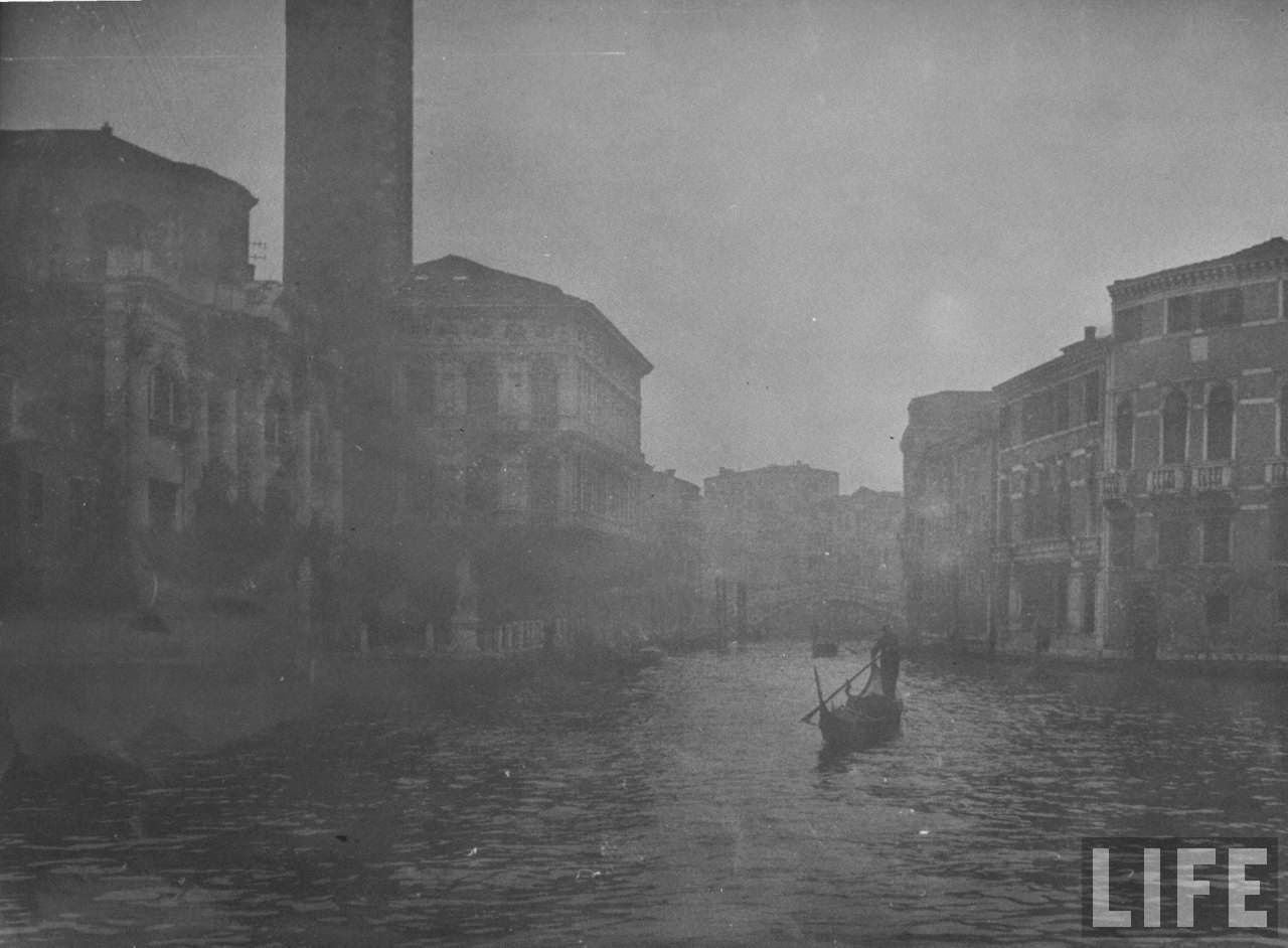 Winter fog hanging over travelers by gondola on Grand Canal amidst the venerable bldgs. of this ancient city.