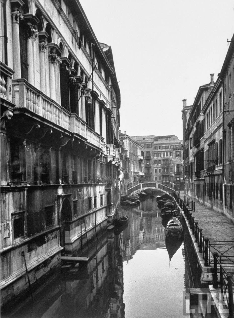 Arched bridge over narrow canal flowing between ancient buildings of the city.